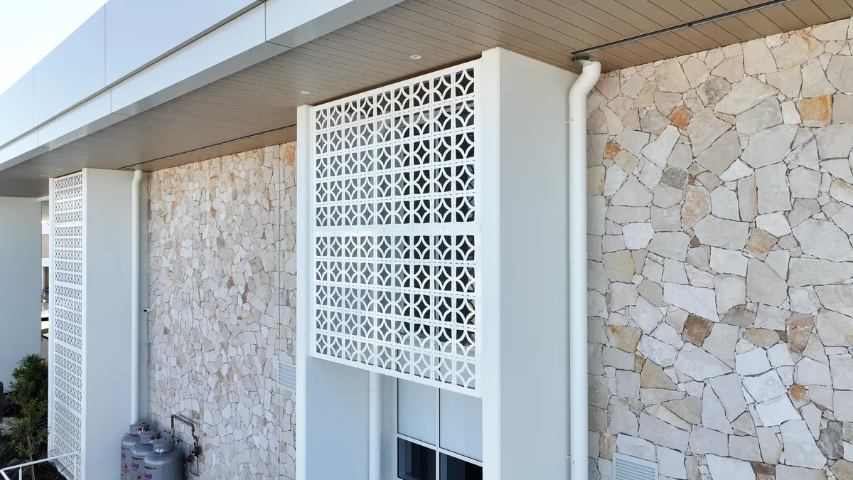 Close detail of a perforated screen panel against the stone facade
