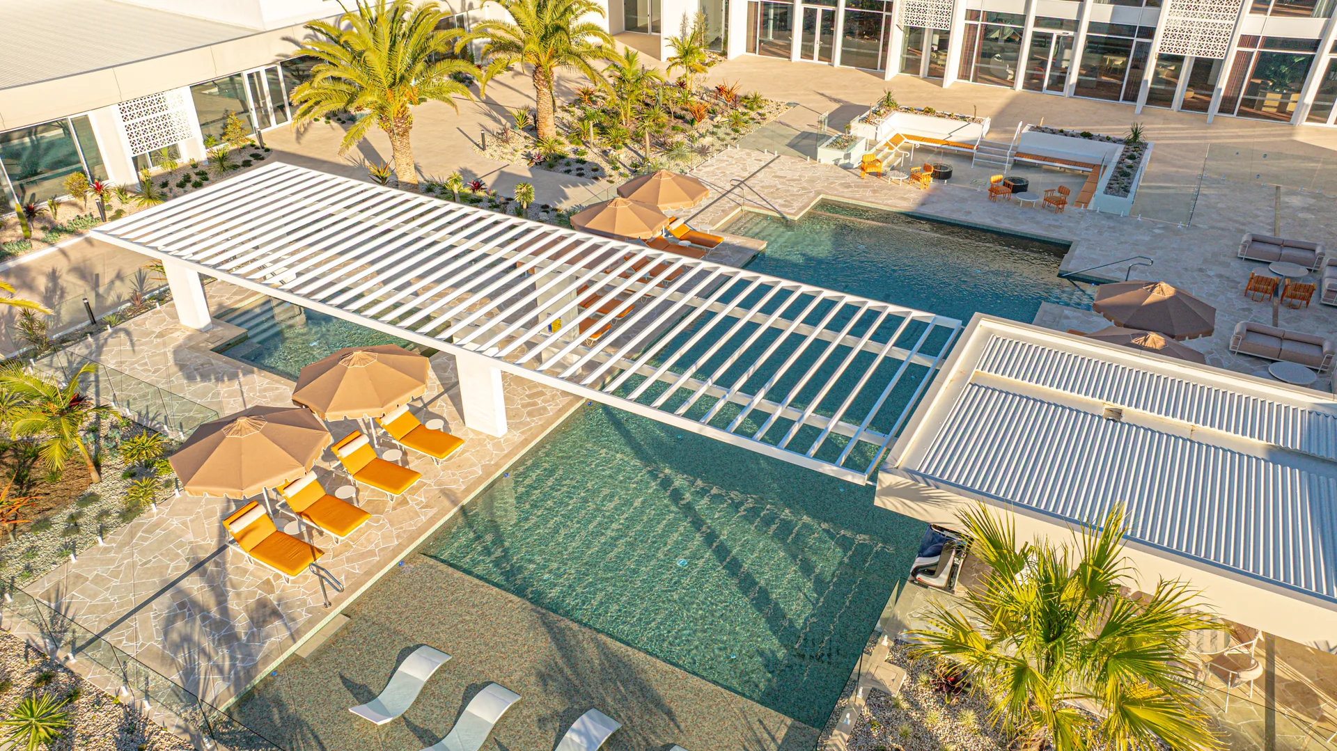 Aerial view of the white aluminium pergola spanning the pool deck at Palm Lake Resort Pelican Waters