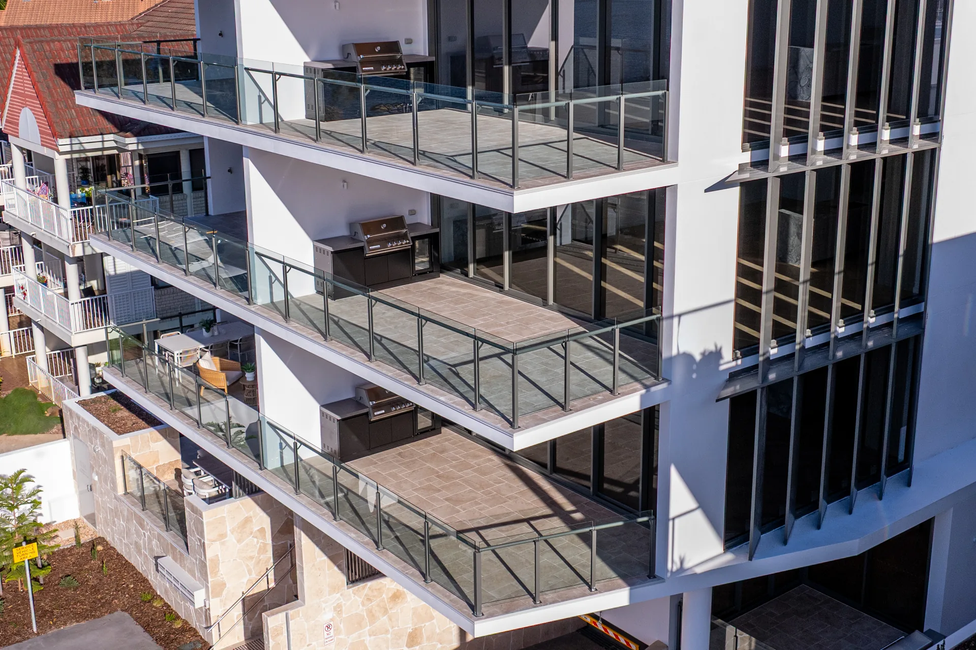 Three levels of frameless glass balustrade along the PRANA balconies, with vertical aluminium privacy screens on the facade beside them