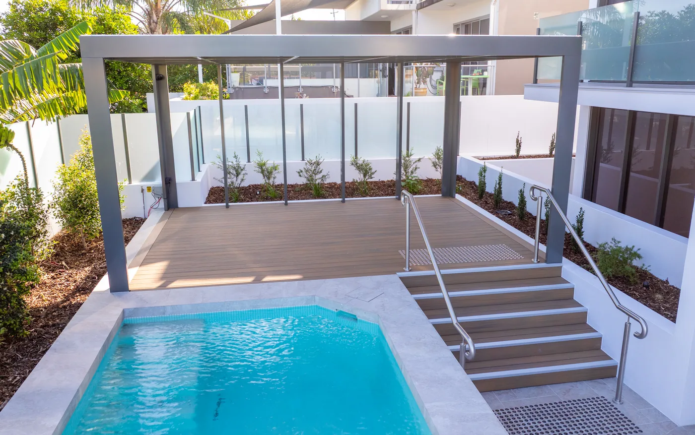 Pool terrace with a pergola overhead, glass balustrade and a stainless steel handrail to the steps